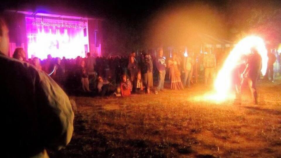 A nighttime outdoor event with a crowd gathered around a performer with a flaming object.