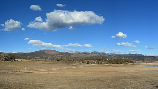 Un vaste paysage ouvert, avec un ciel bleu dégagé, des montagnes lointaines et un petit plan d’eau.