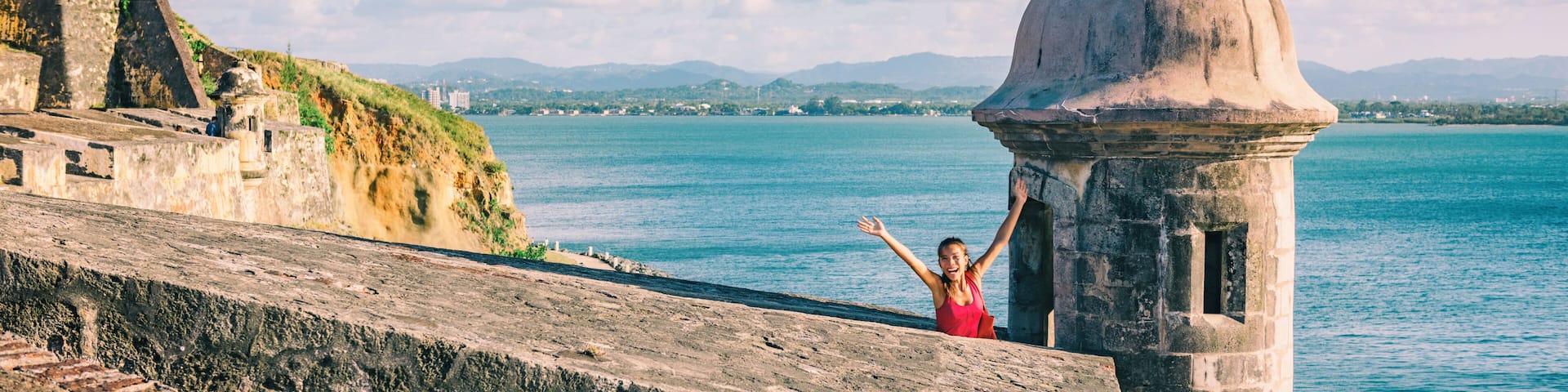 San Juan Puerto Rico travel happy tourist woman waving open arms in happiness at watch tower of Castillo San Felipe del Morro panoramic banner background.