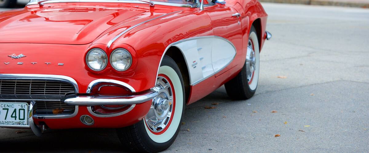 A vintage red convertible car with white racing stripes and chrome accents.