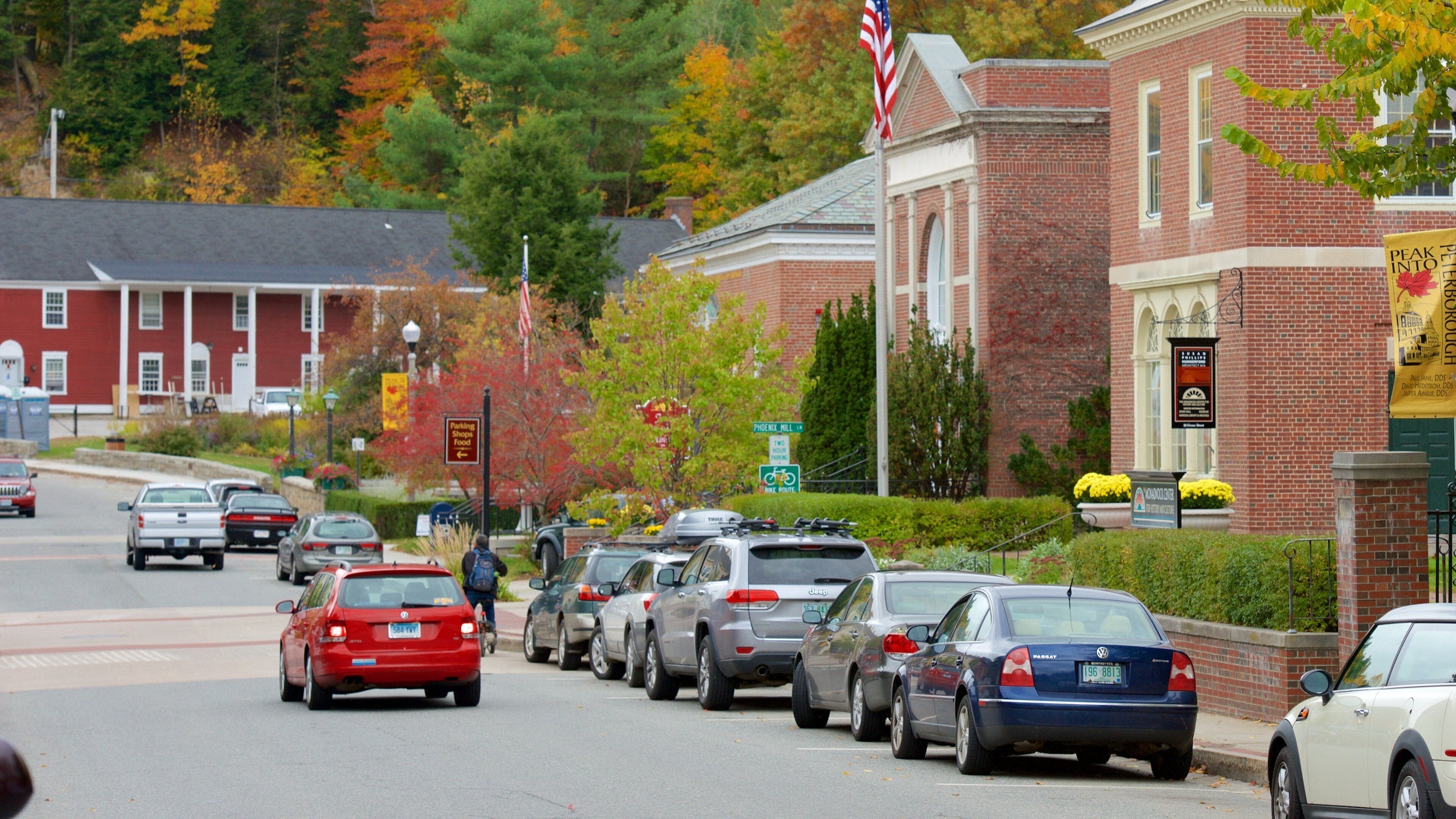 A street lined with parked cars, a brick building, and autumn foliage.