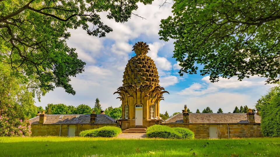 A stone building with a pineapple-shaped tower, surrounded by lush greenery and a clear sky.