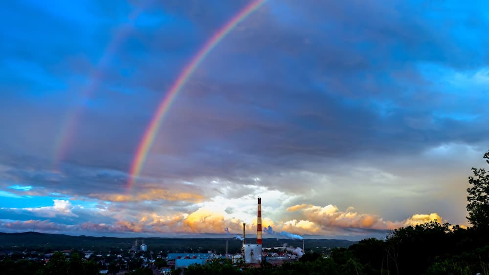 A rainbow over a landscape with industrial structures and a cloudy sky.
