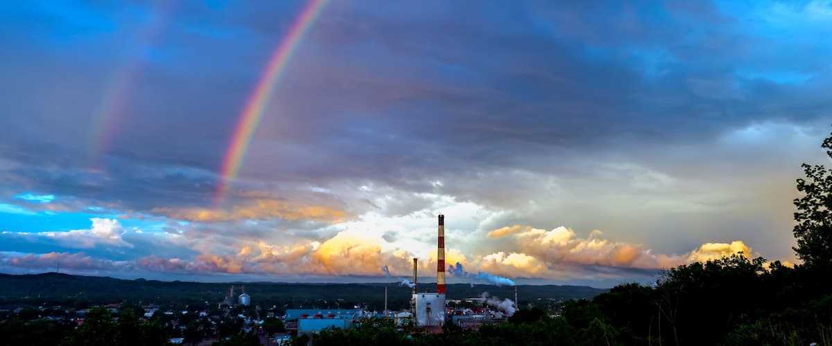 A rainbow over a landscape with industrial structures and a cloudy sky.