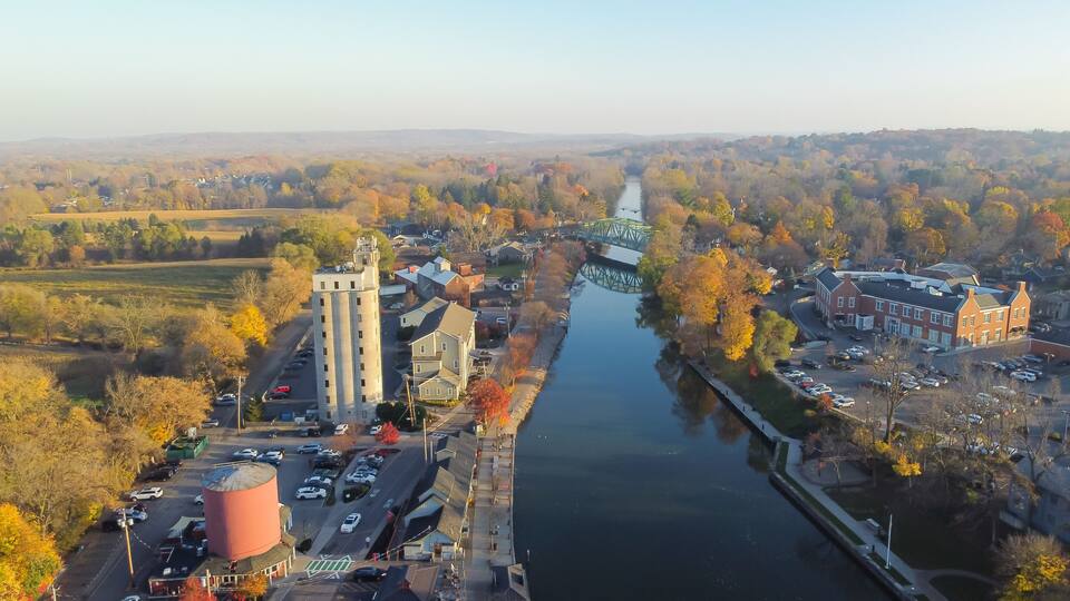 An aerial view of a town with a river, a bridge, and autumn-colored trees.