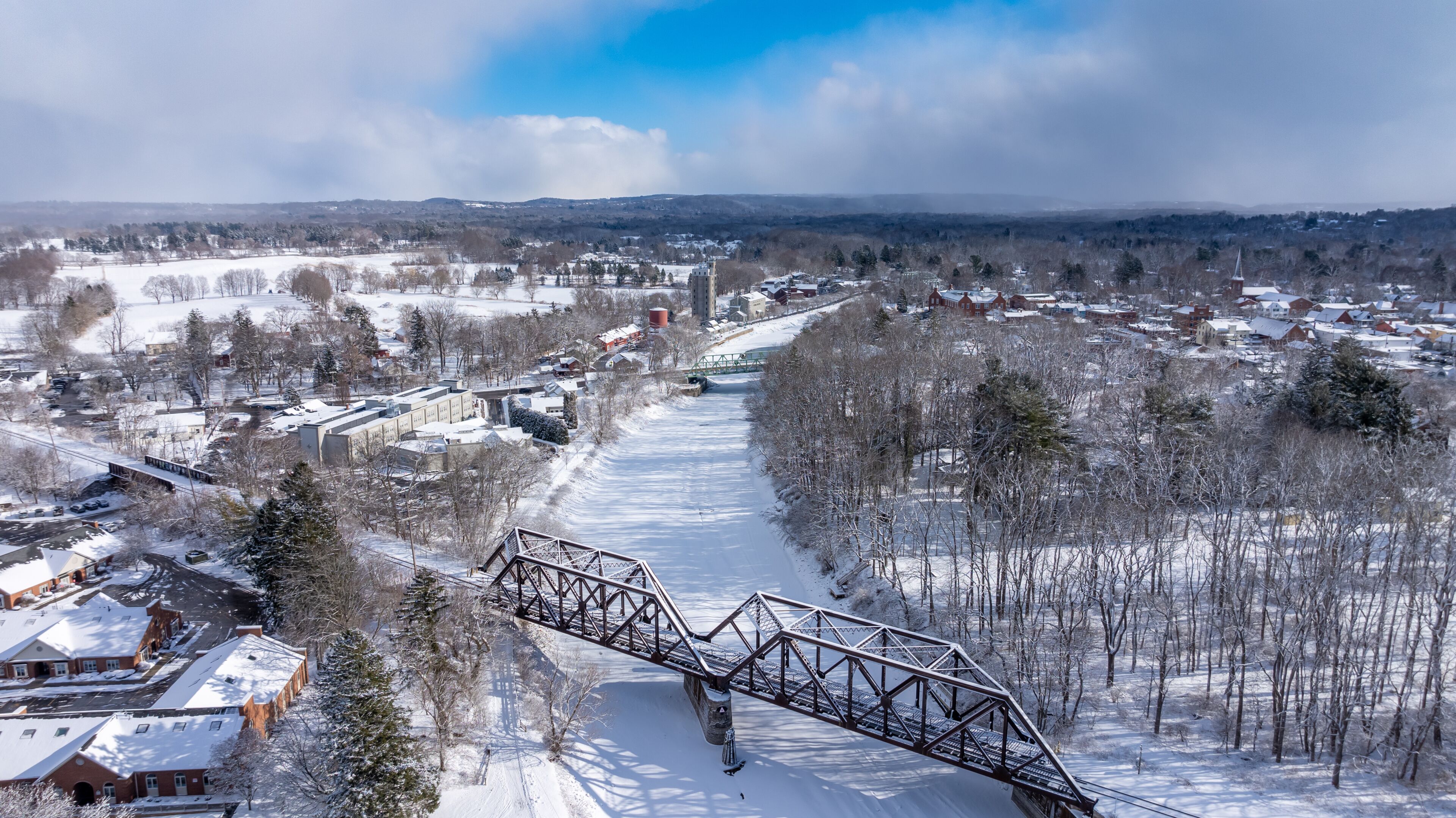 A snow-covered landscape with a bridge, buildings, and a river.