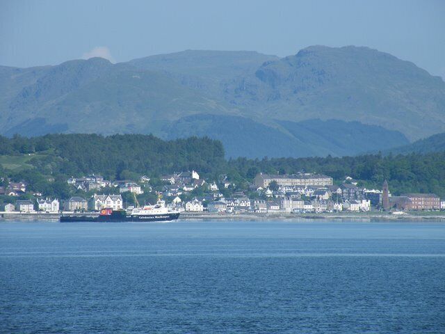 A coastal town with a ferry, houses, and mountains in the background.