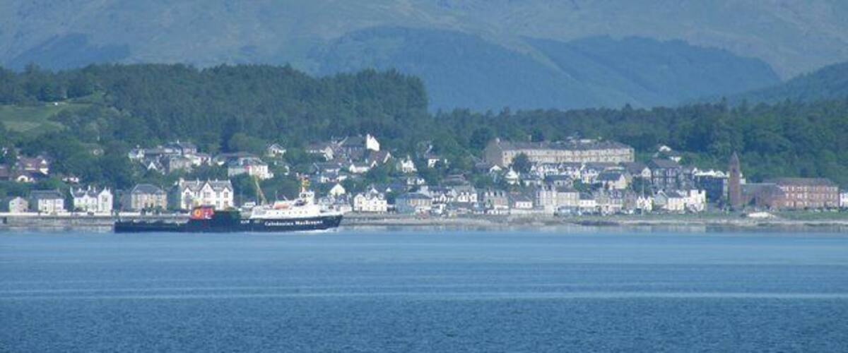 Un pueblo costero con un ferry, casas y montañas al fondo.