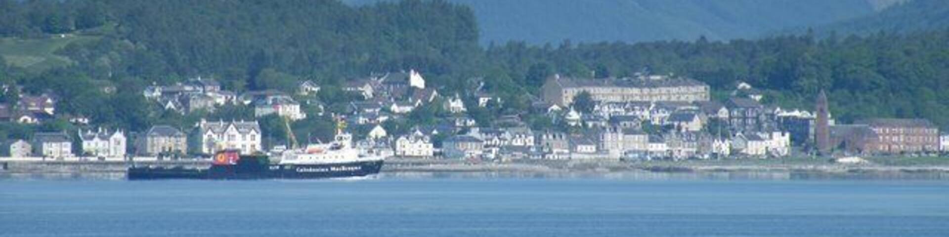 A coastal town with a ferry, houses, and mountains in the background.