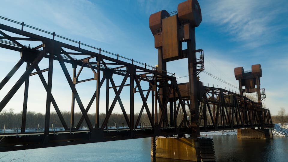 A large steel bridge over a river with snow on the ground.