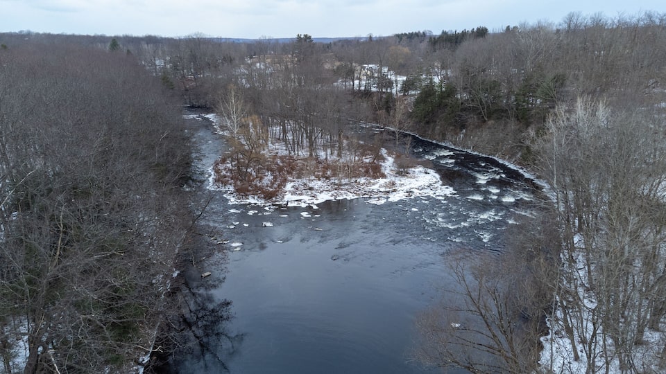 A river flowing through a forested area with snow patches on the ground.