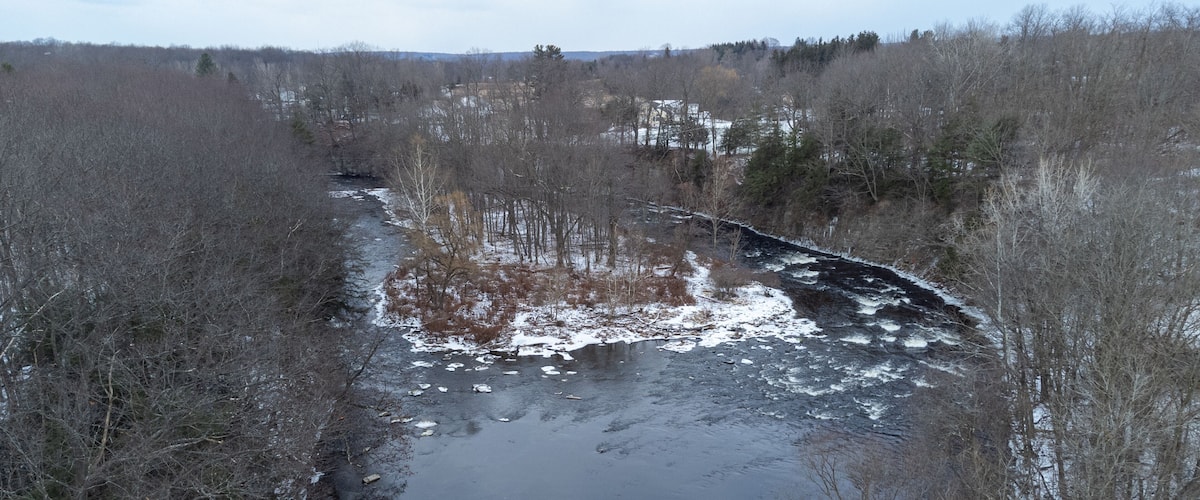 A river flowing through a forested area with snow patches on the ground.