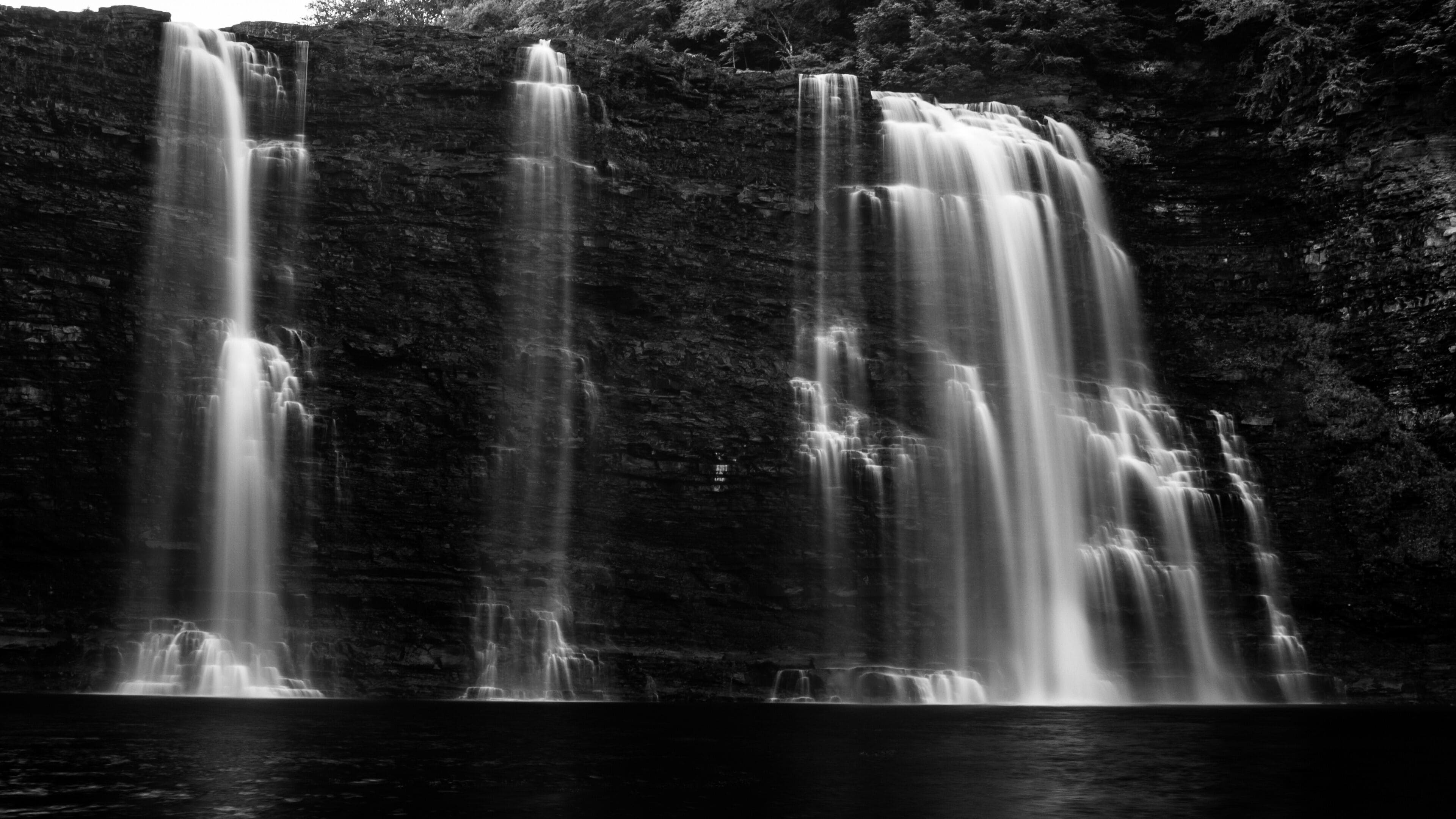 A multi-tiered waterfall cascading over a rocky cliff into a body of water.