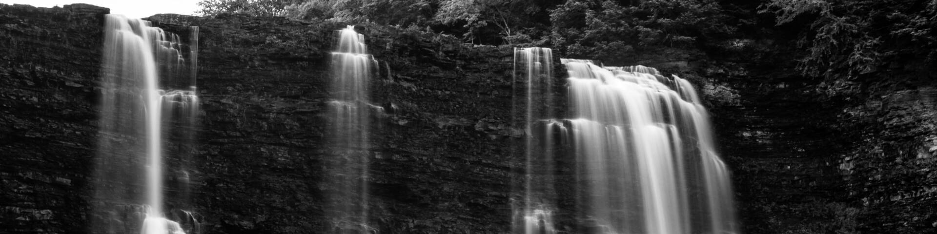 A multi-tiered waterfall cascading over a rocky cliff into a body of water.