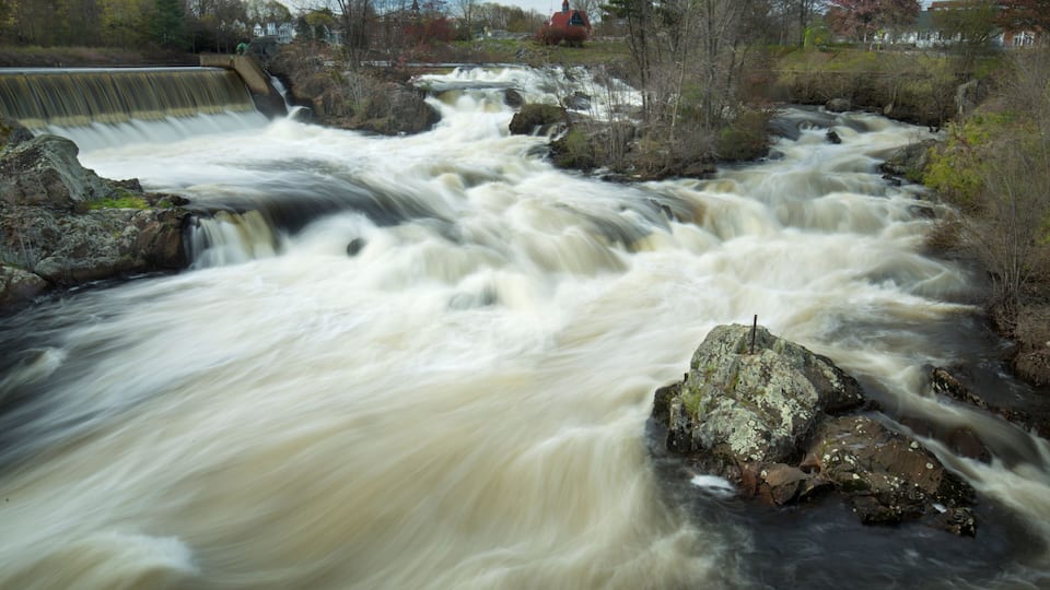 A fast-flowing river with a dam and rocky terrain.
