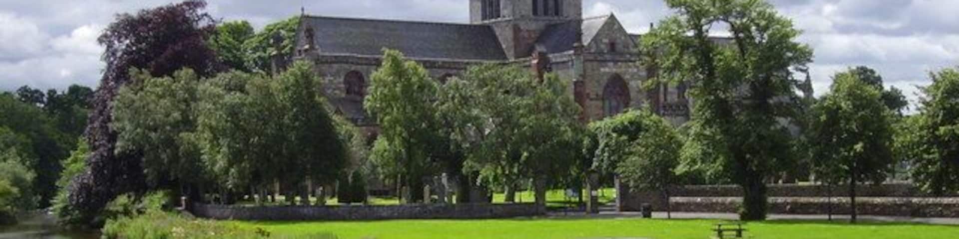 A historic building with a tower, surrounded by a pond and lush greenery.