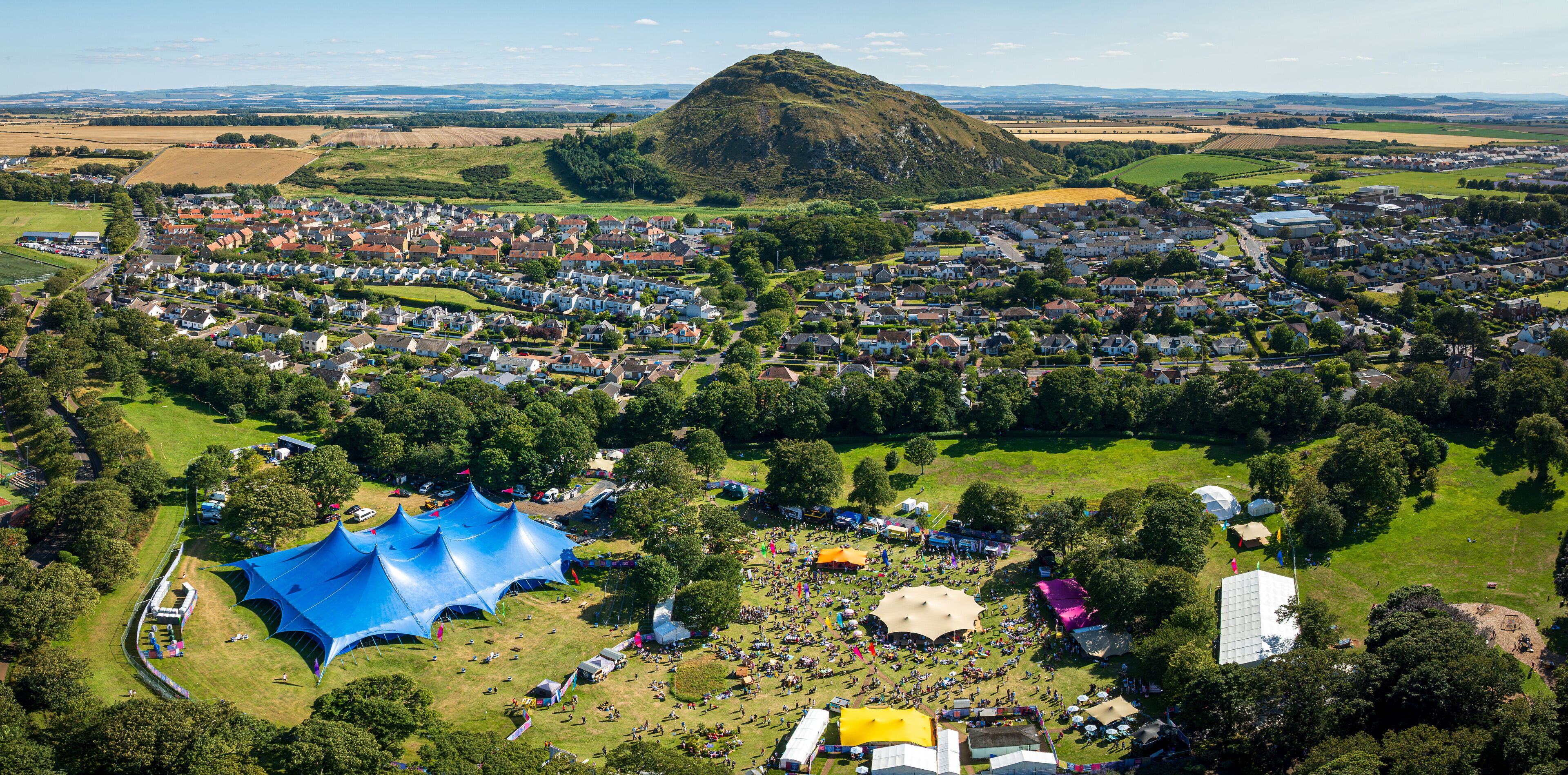 Aerial view of a vibrant festival with colorful tents and bustling crowds set against the backdrop of a lush green landscape, Haddington, Scotland, United Kingdom.