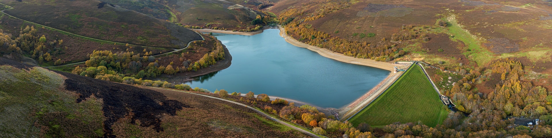 Aerial view of a reservoir's tranquil waters reflect the sky, embraced by the rugged hillsides and vibrant autumn foliage, Haddington, Scotland, United Kingdom.