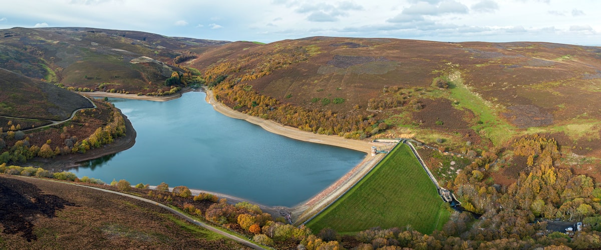 A lake surrounded by hills with a road and a small building near the water.