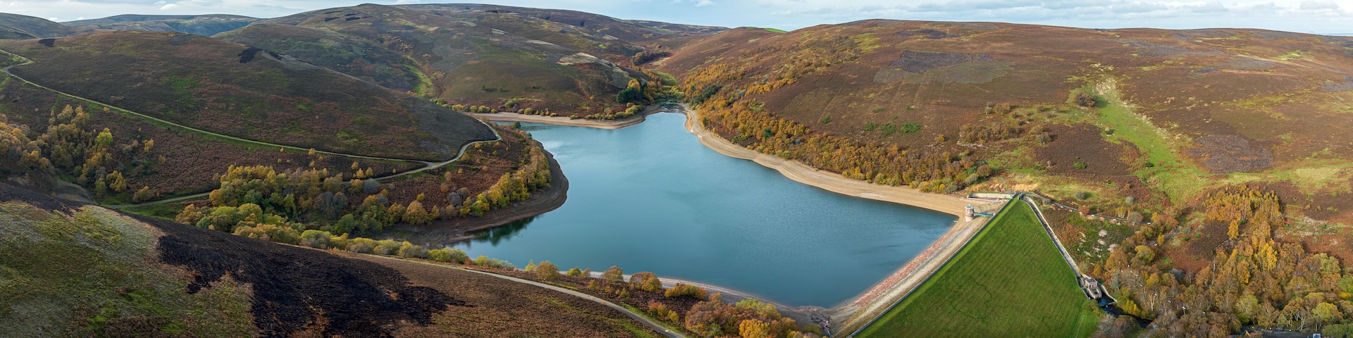 A lake surrounded by hills with a road and a small building near the water.