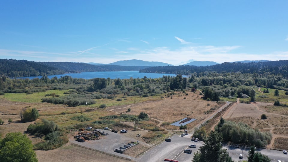 A lake surrounded by forested hills, a parking area, and a dirt road.
