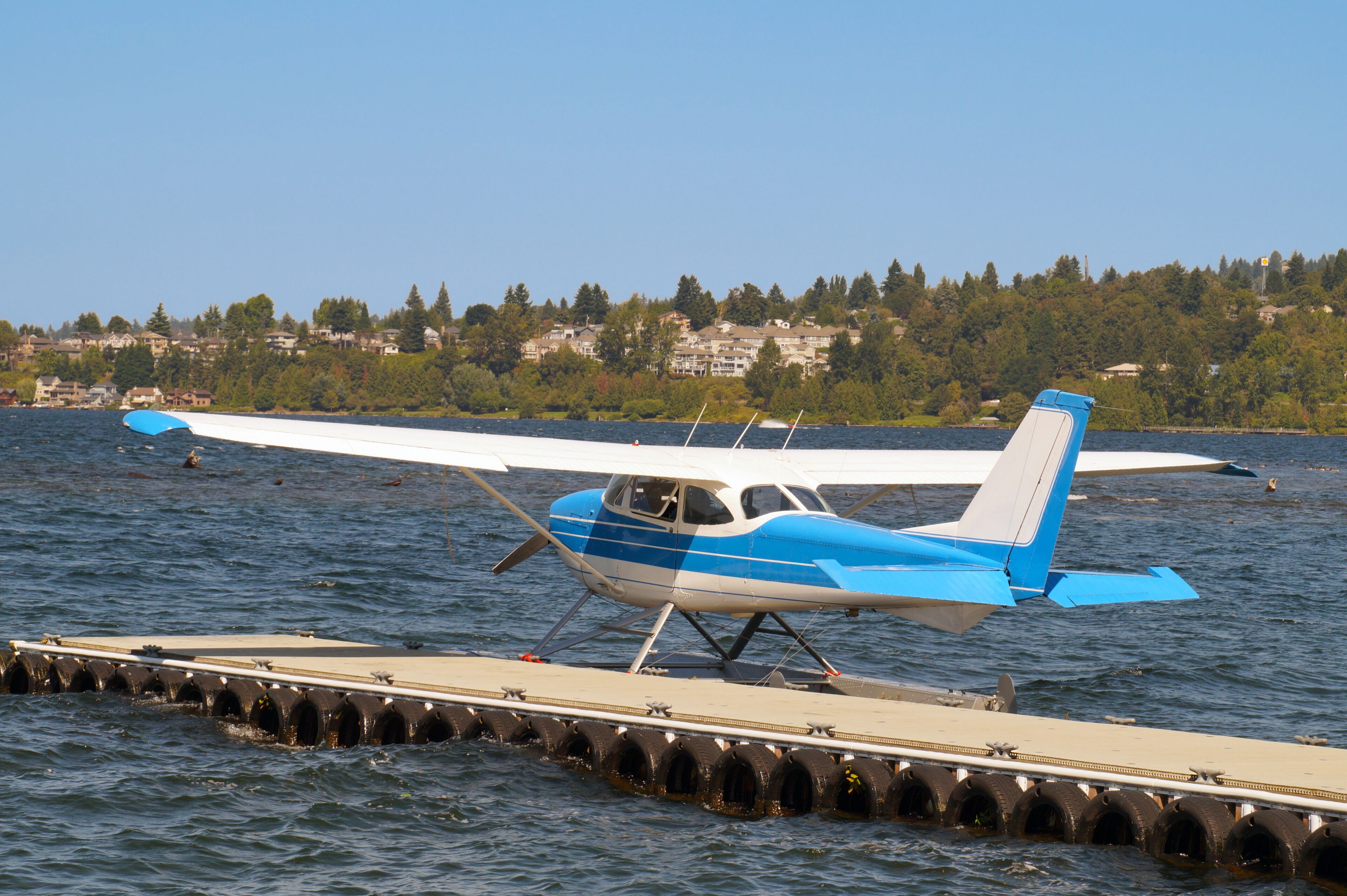 A seaplane on a dock with a lake and houses in the background.