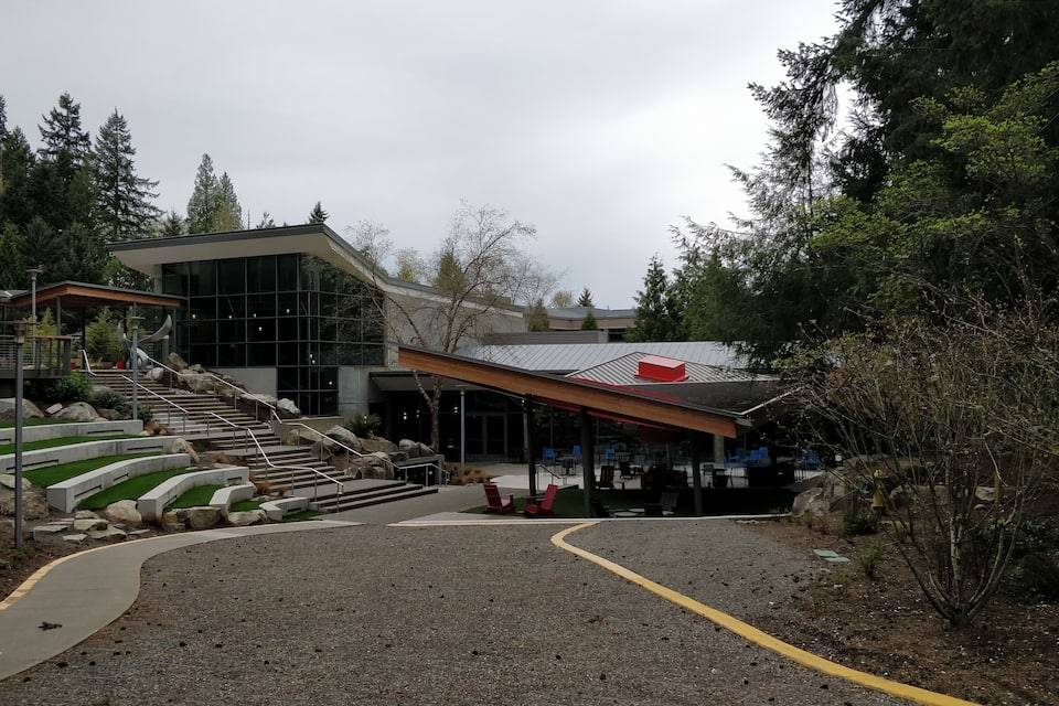 A modern building with a glass facade, a red roof, and a set of outdoor stairs leading to a covered area with seating.