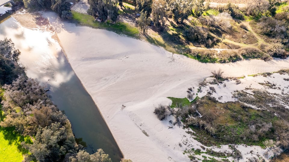 An aerial view of a river with a snow-covered area and surrounding vegetation.