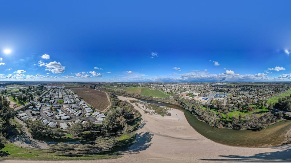 An aerial view of a town with a river, green fields, and a large industrial area.
