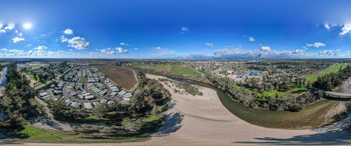 An aerial view of a town with a river, green fields, and a large industrial area.