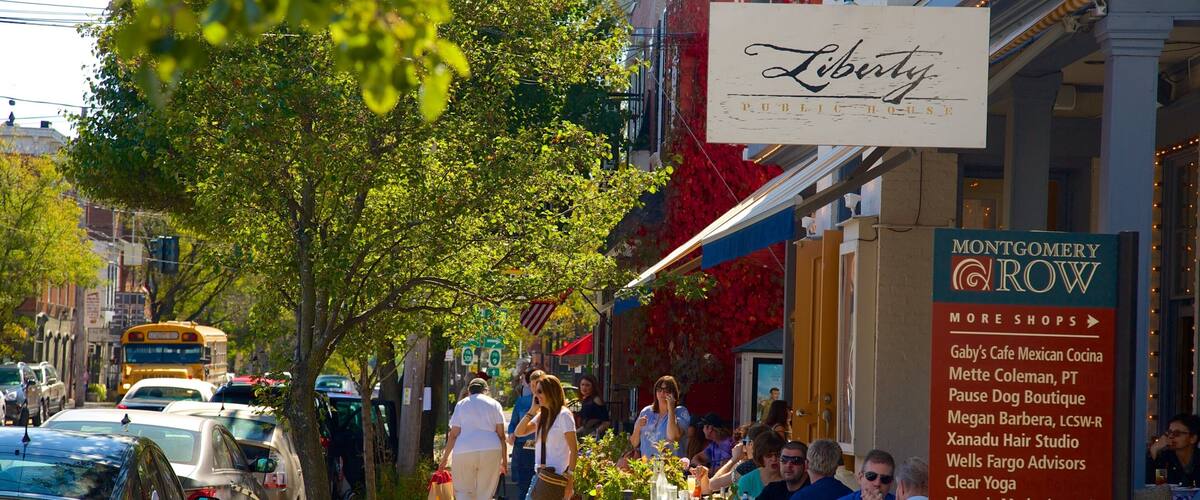 A busy street with parked cars, pedestrians, and outdoor seating at a restaurant.