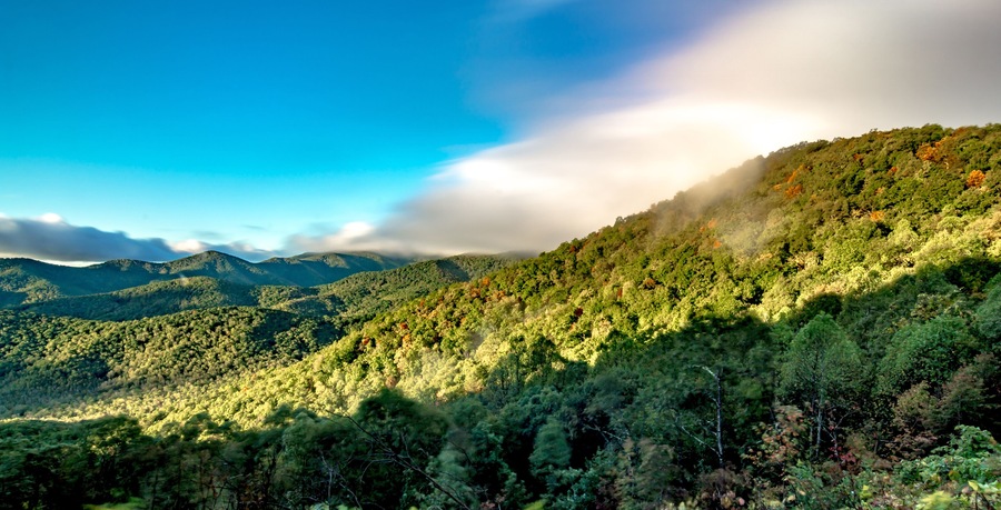 A mountainous landscape with dense forests and a clear blue sky.