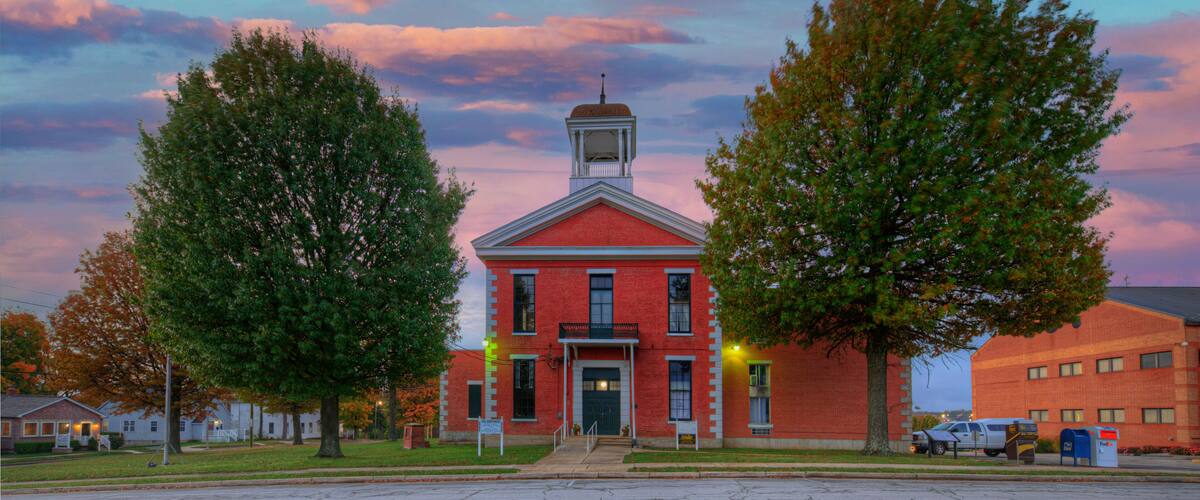 A red brick building with a bell tower, surrounded by trees and a clear sky.