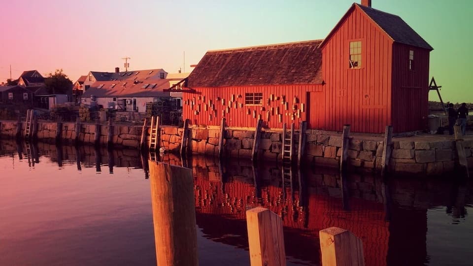 A red wooden building by a calm water body with a stone dock and a clear sky.