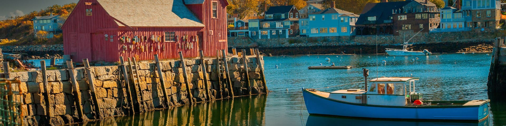 A harbor with a red building, a blue boat, and houses in the background.