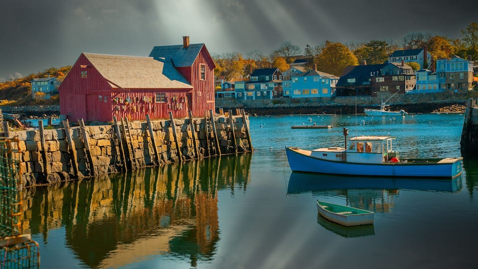 A harbor with a red building, a blue boat, and houses in the background.