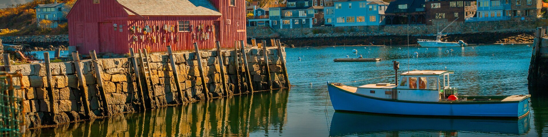 Un puerto con un edificio rojo, un bote azul y casas al fondo.
