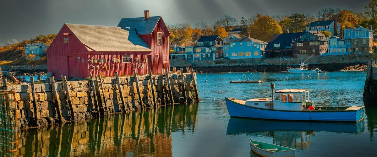 A harbor with a red building, a blue boat, and houses in the background.