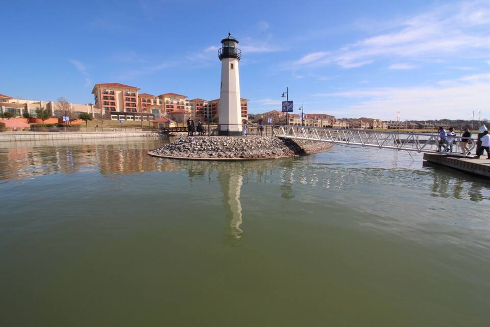 A lighthouse on a small island, surrounded by water, with buildings in the background.