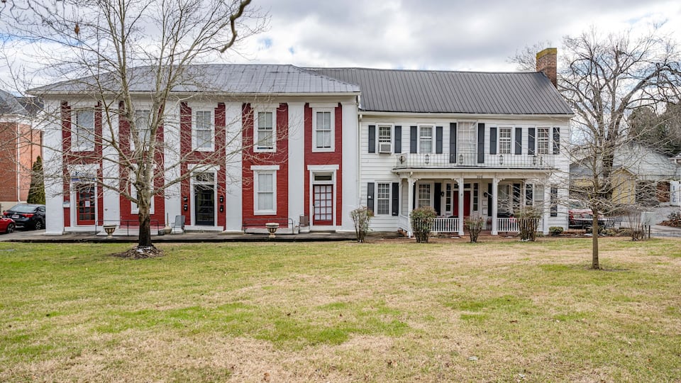 A large, two-story red and white house with a porch and a brick chimney.