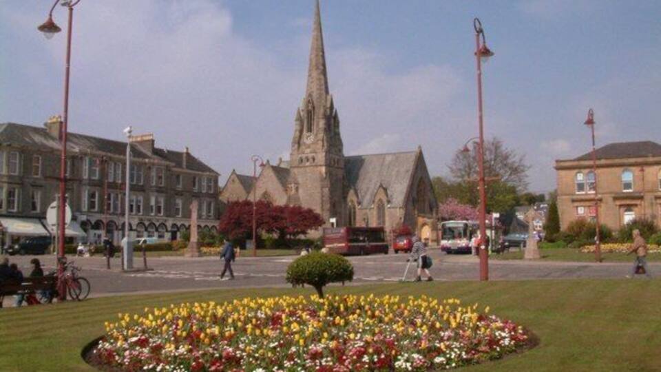 A town square with a church steeple, flower beds, and buildings.