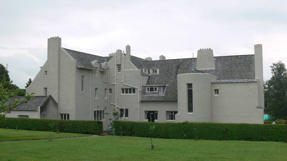 A large, historic building with a steeply pitched roof and multiple chimneys.