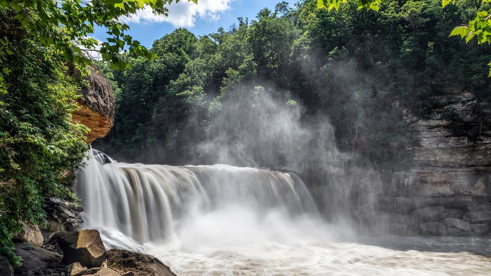 A waterfall cascading over a rocky cliff surrounded by dense green foliage.