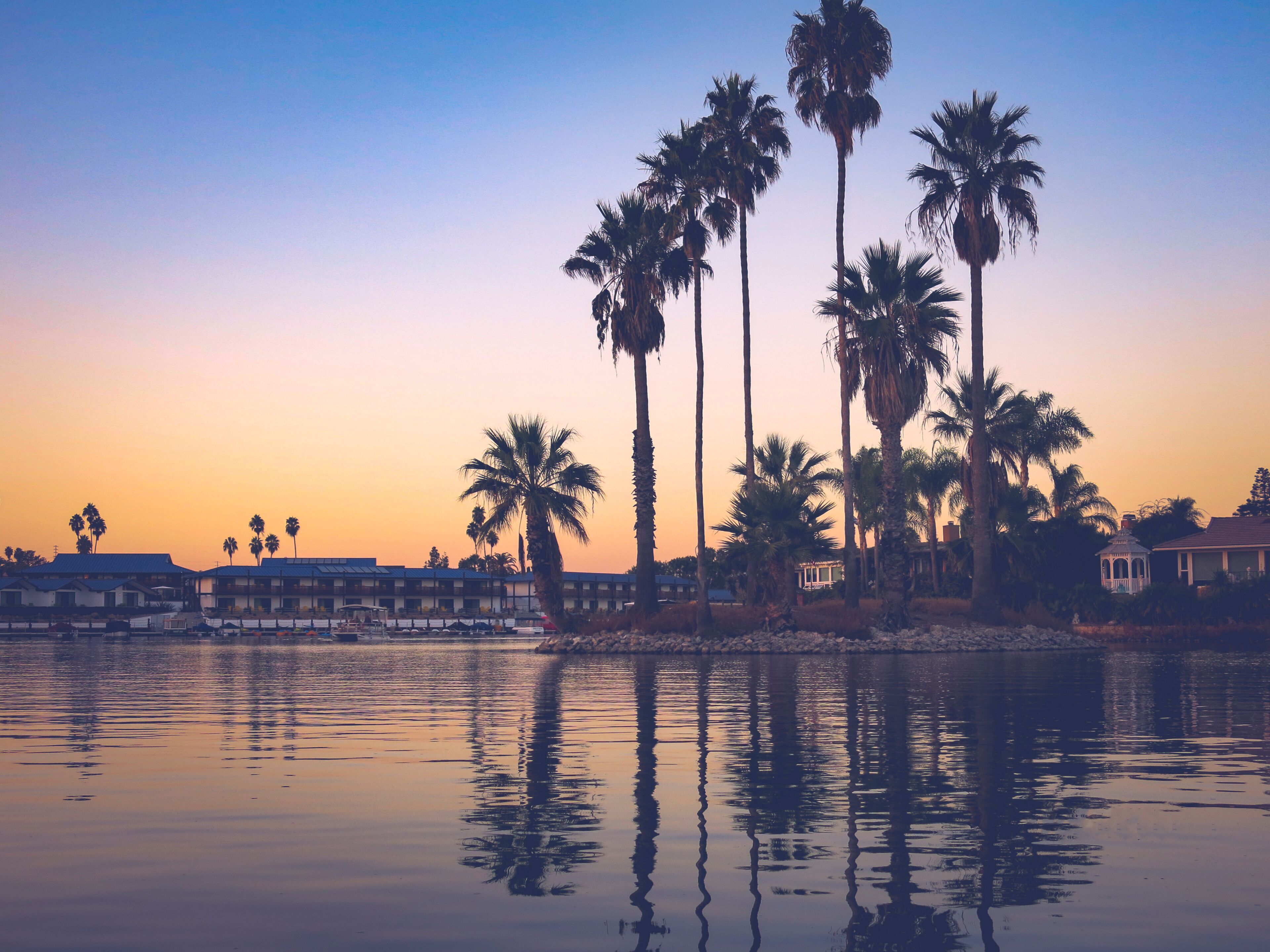 Sunset time in Lake San Marcos, North County, CA. Great reflections over the lake and the sky is in blue and orange colour with high palm tree silhouettes. Reflections are in focus only.