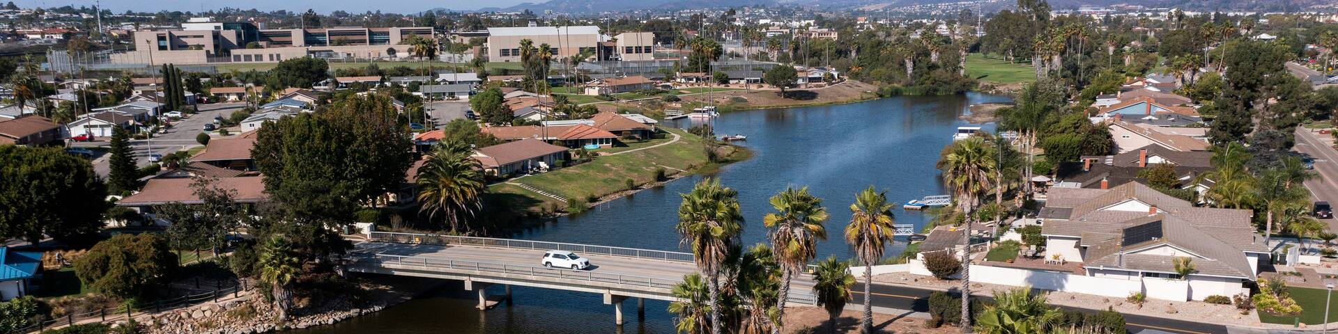 A residential area with a bridge over a river, surrounded by houses and palm trees.