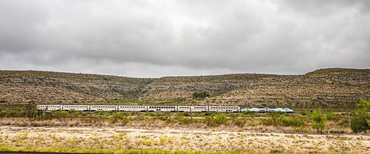 A train traveling through a desert landscape with sparse vegetation and rocky hills.