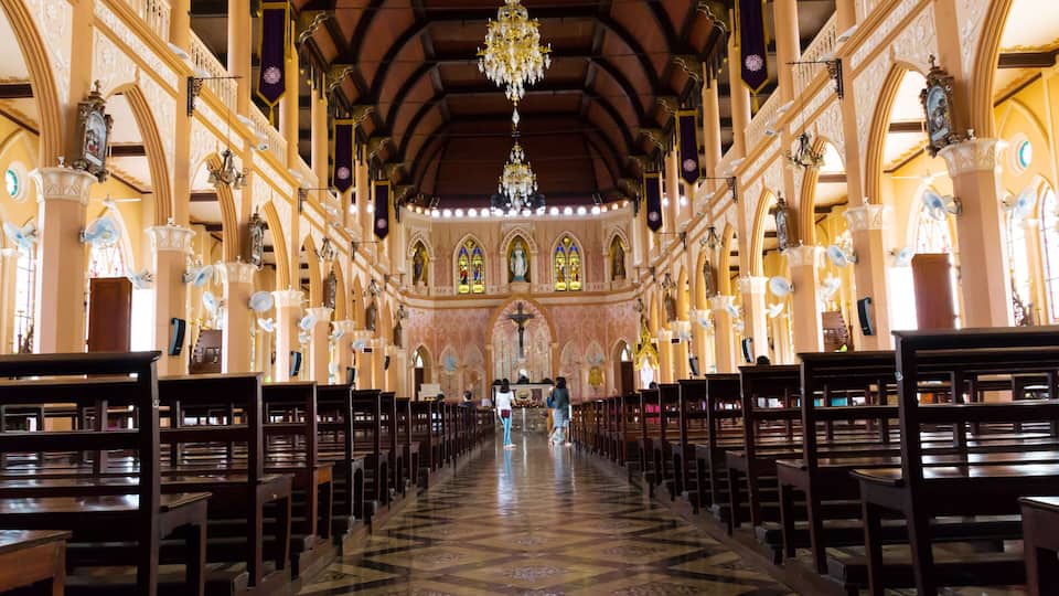 An ornate church interior with a high ceiling, chandeliers, and rows of pews.