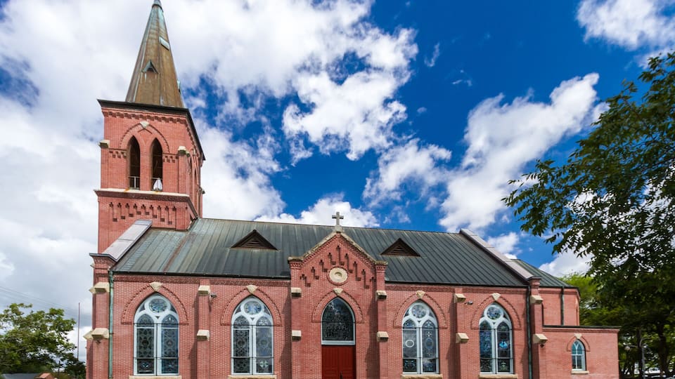 A red brick church with a tall steeple and large arched windows.