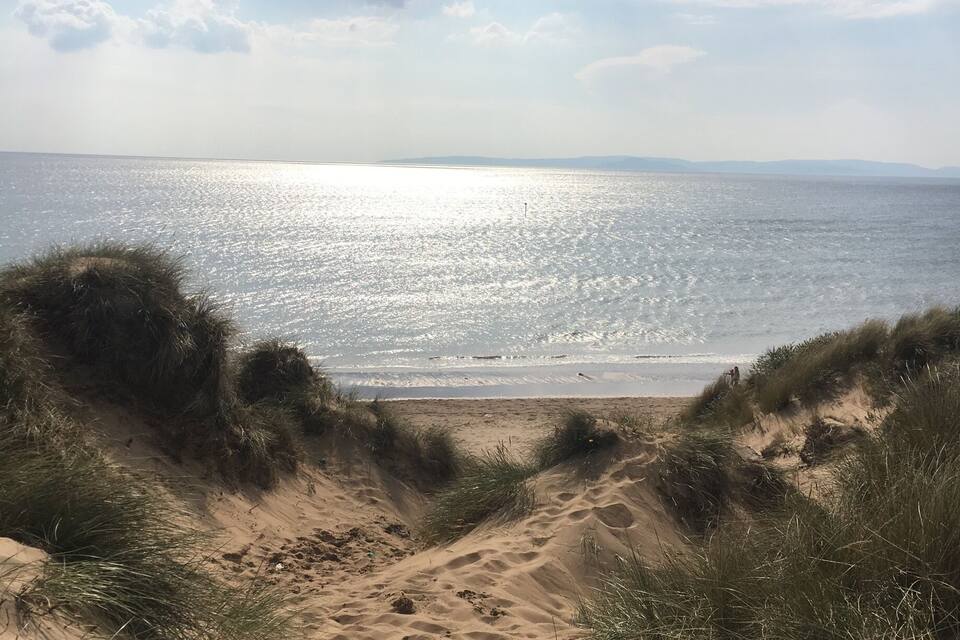 A sandy beach with dunes and a calm sea under a partly cloudy sky.