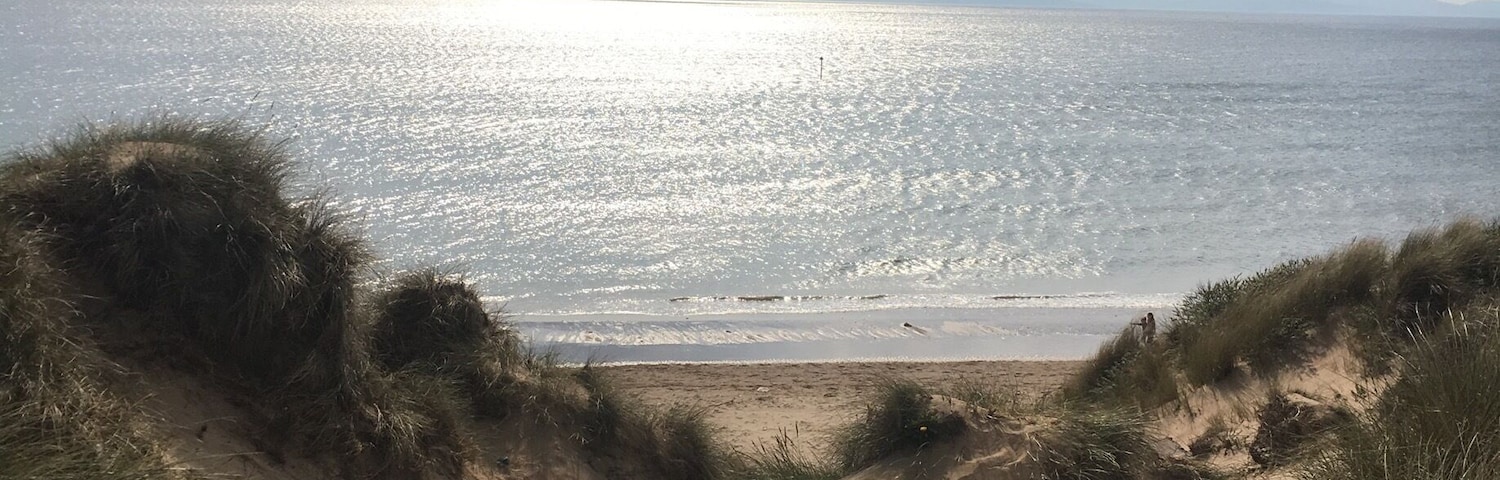 A sandy beach with dunes and a calm sea under a partly cloudy sky.